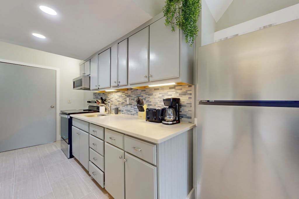 A modern kitchen with grey cabinets, a stainless steel refrigerator, and a tiled backsplash.