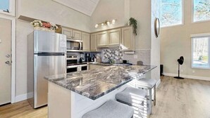 A modern kitchen with a large island, stainless steel appliances, and a view of the outdoors.