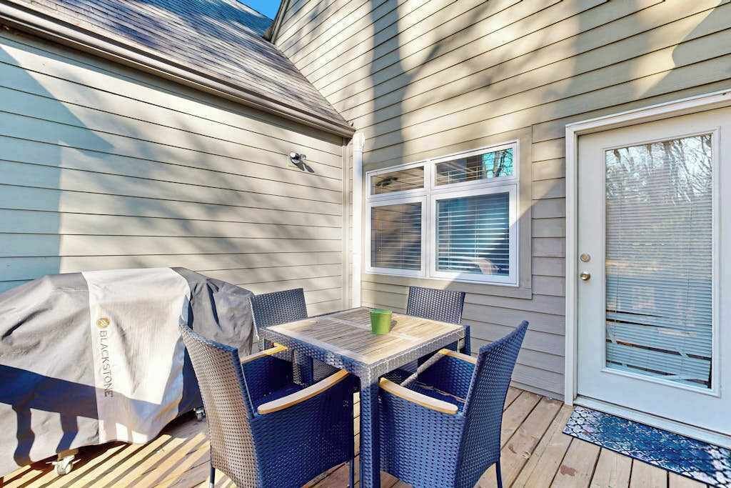 Un patio couvert avec une table et des chaises, un barbecue abrité et une porte avec une fenêtre.