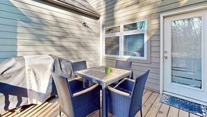 A covered patio with a table and chairs, a covered grill, and a door with a window.