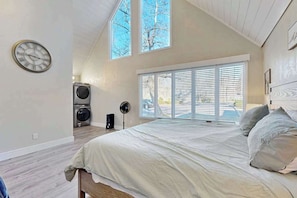 A bedroom with a bed, a clock, a window with blinds, a fan, and a washing machine. - Charming Sapphire, NC Condo: Cozy, Dog-Friendly, Pool, Golf Course, & More (Sapphire)