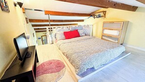 Een slaapkamer met een bed, een bureau met een computer, een kapstok en een houten plafond.