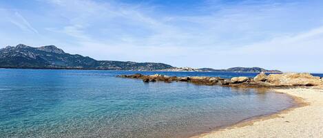 A beach with clear water, rocky shoreline, and distant mountains.