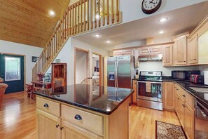 A kitchen with wooden cabinets, a stainless steel refrigerator, and a wooden staircase.