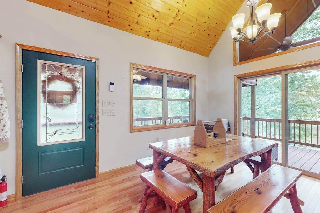 A wooden dining table with benches, large windows, a door with a glass panel, and a chandelier.