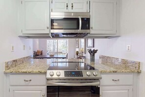 A kitchen with white cabinets, a stainless steel microwave, a stove, and granite countertops.