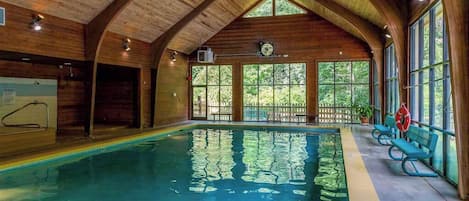 Una piscina interior con vigas de madera, ventanas amplias y un flotador.
