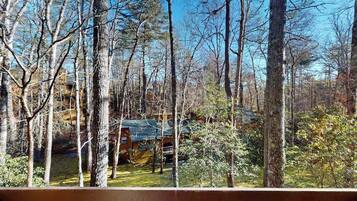 Une terrasse en bois donnant sur une zone boisée, avec un chalet à proximité.