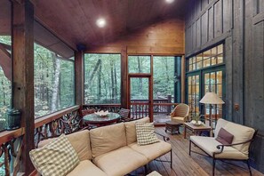 Eine Holzterrasse mit einer Couch, Stühlen und einem Tisch mit Blick auf einen Wald.