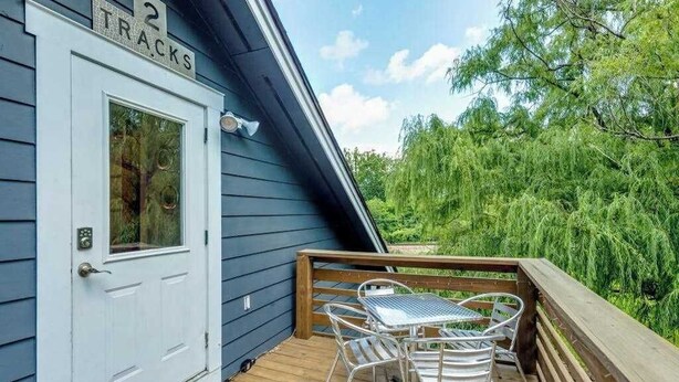 Een houten terras met een witte deur waarop '2 TRACKS' staat, een metalen tafel met stoelen en uitzicht op weelderige begroeiing.