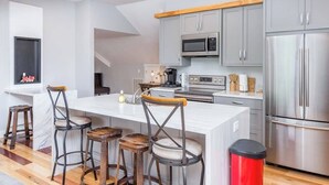 Een moderne keuken met grijze kastjes, roestvrijstalen apparatuur en een wit kookeiland met barkrukken.