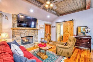 A cozy living room with a stone fireplace, a television mounted above it, a comfortable sofa, and a wooden door. - Stylish dog-friendly cottage with modern feel, fast WiFi, ideal location & more (Swannanoa)