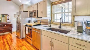 A kitchen with wooden flooring, stainless steel appliances, a window with blinds, and a wooden ceiling. - Stylish dog-friendly cottage with modern feel, fast WiFi, ideal location & more (Swannanoa)