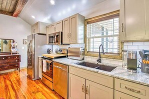 A kitchen with wooden flooring, stainless steel appliances, a window with blinds, and a wooden ceiling. - Stylish dog-friendly cottage with modern feel, fast WiFi, ideal location & more (Swannanoa)