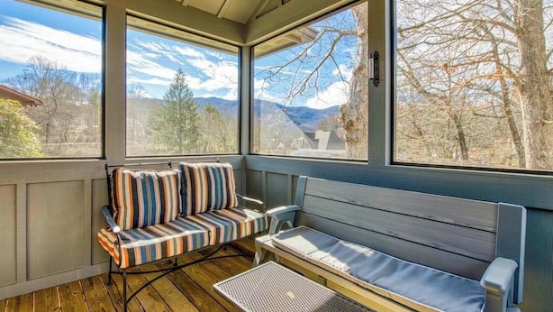 A sunroom with large windows, a cushioned bench, and a small table. - Stylish dog-friendly cottage with modern feel, fast WiFi, ideal location & more (Swannanoa)