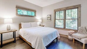 Quarto com cama, duas mesas de cabeceira, uma cadeira, janela com persianas e ventilador de teto.