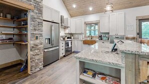 Cozinha moderna com bancadas de granito, eletrodomésticos de aço inoxidável e uma parede decorativa em pedra.