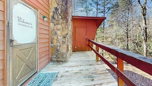 A wooden deck leading to a stone wall entrance with a red door and a welcome sign. - Once Upon a Cabin, Mountain Views (Murphy)