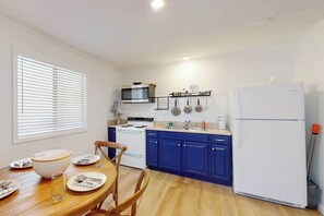 Une cuisine compacte comprenant une table à manger, un réfrigérateur blanc, des placards bleus et un four à micro-ondes.