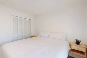 Une chambre à coucher comprenant un lit, une table de chevet, une étagère en bois et une armoire.