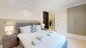 Ein ordentlich eingerichtetes Hotelzimmer mit einem großen Bett, zwei Nachttischen mit Lampen, einem Kleiderschrank und einem Spiegel.