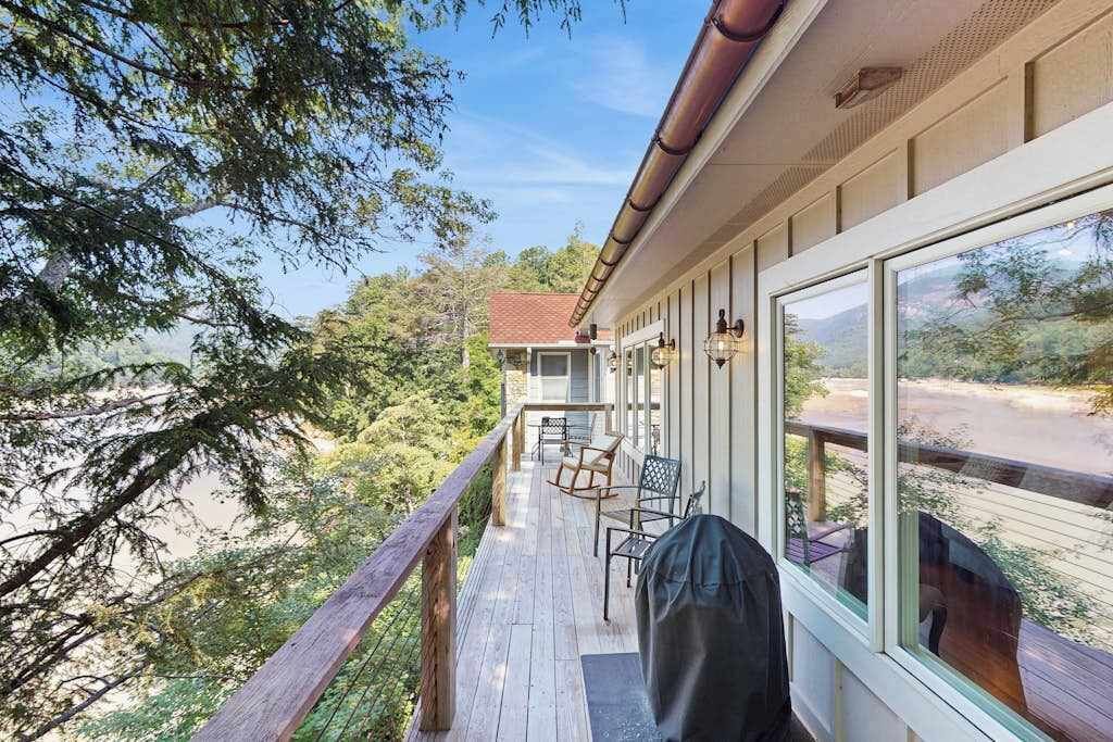 Une terrasse en bois, dotée de mobilier d’extérieur, de grandes fenêtres et offrant une vue sur le paysage environnant.