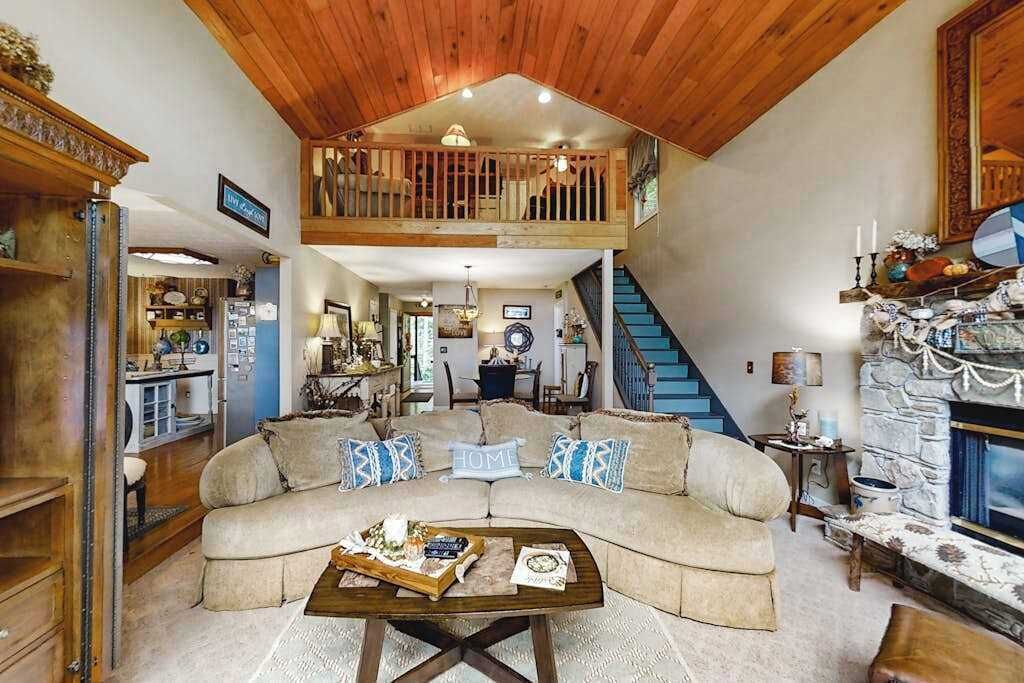 Un salon spacieux avec un haut plafond, un escalier en bois, une cheminée en pierre et un coin salon confortable.