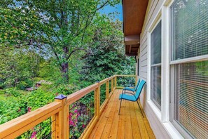 Eine Holzterrasse mit Geländer, zwei blaue Stühle und Blick auf einen Garten mit Bäumen und Sträuchern.