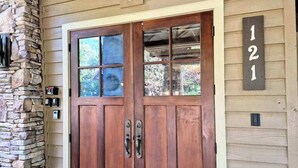 Una puerta doble de madera con paneles de vidrio, un pilar de piedra y un cartel con el número de la casa.