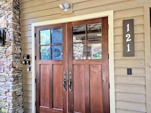 A wooden double door with a stone pillar, a mailbox, and a house number sign.