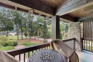 A covered outdoor area with a table and chairs, a stone wall, and a view of a landscaped area with trees.