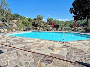 A swimming pool with stone tiles, lounge chairs, and red umbrellas.
