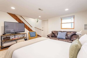 Ein Schlafzimmer mit einem Bett, einem Fernseher auf einem Schrank, einem braunen Ledersofa, einem Fenster und einer Treppe.