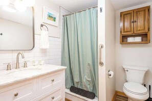 Ein Badezimmer mit einem weißen Waschbecken, einem Spiegel, einer Duschvorhang und Holzschränken über dem WC.
