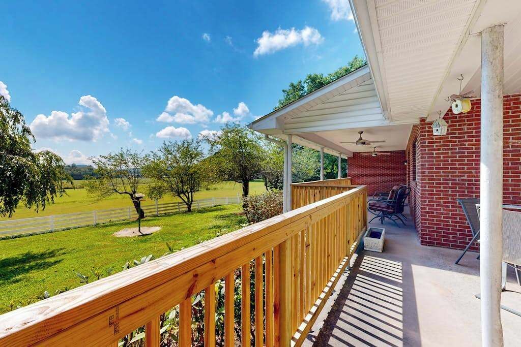 Un espace extérieur abrité doté d’une terrasse en bois, d’un mur en briques et offrant une vue sur un paysage verdoyant.