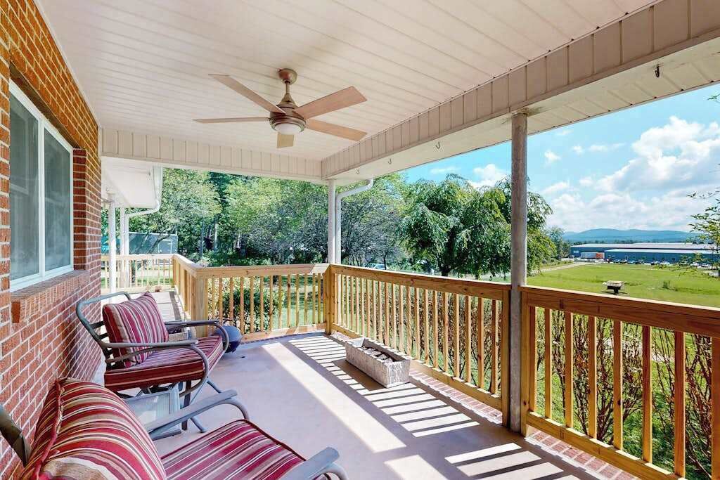 A covered porch with a ceiling fan, a brick wall, and a view of a green landscape.