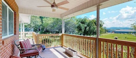 A covered porch with a ceiling fan, a brick wall, and a view of a green landscape.