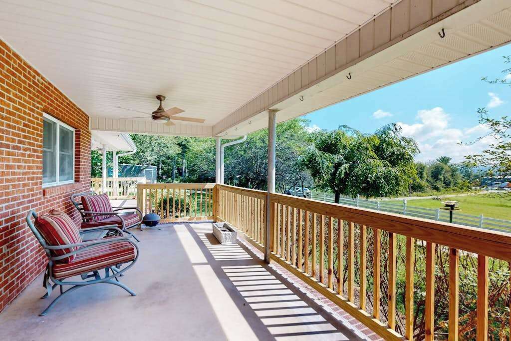 A covered porch with a brick wall, a ceiling fan, and a view of a green landscape.
