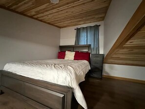 A bedroom with a wooden ceiling, a bed with a white bedspread, a nightstand, and a window with curtains. - Newly built spacious 2BDR cabin - 6A (Terrace)