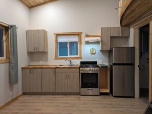 Une cuisine avec des meubles en bois, un réfrigérateur en acier inoxydable, une cuisinière et une fenêtre avec des stores.
