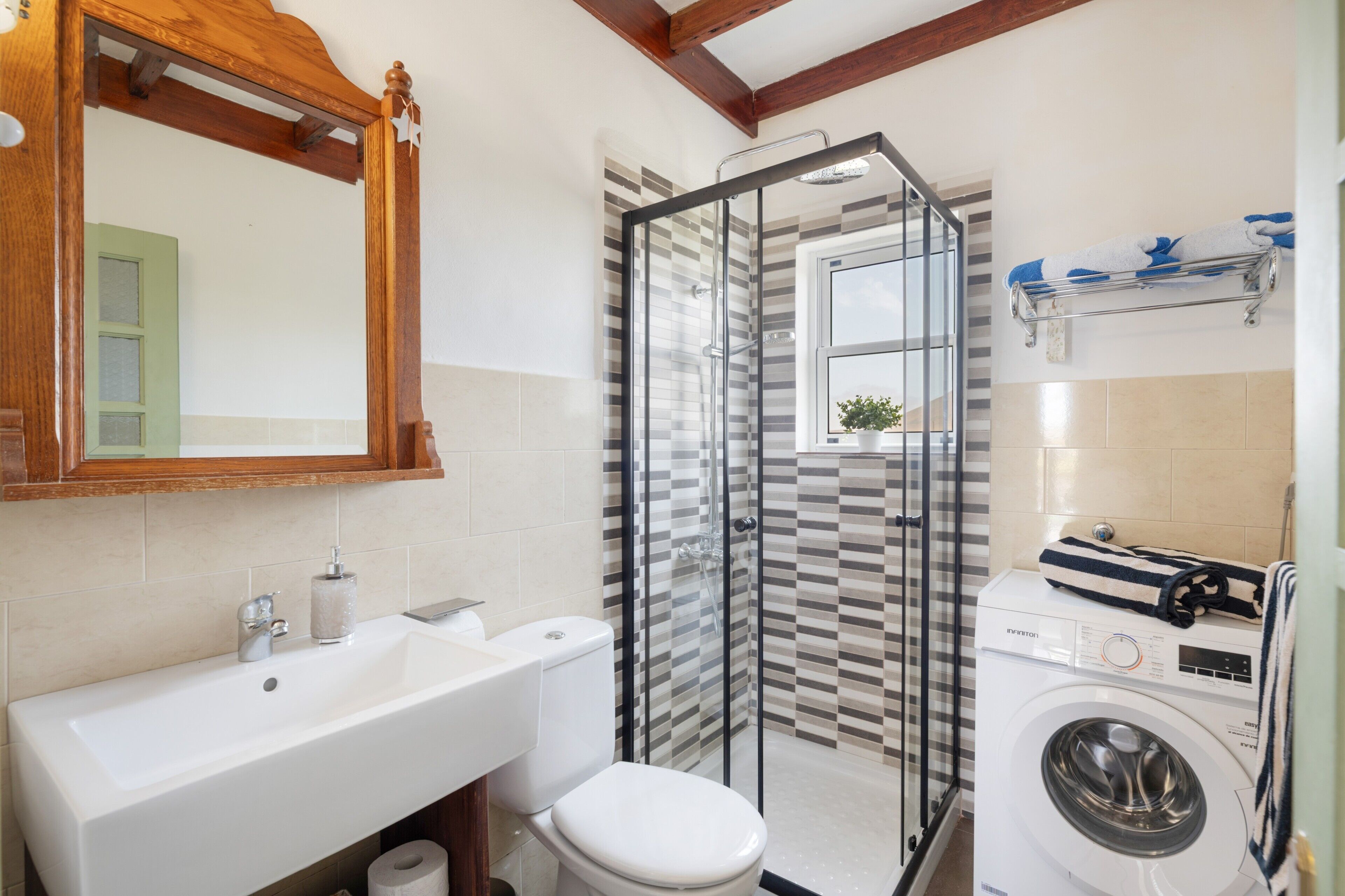 A bathroom with a sink, toilet, shower, and washing machine.