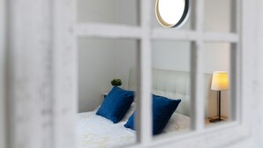 Un dormitorio con cama, almohadas, mesita de noche, lámpara y espejo.