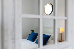 Een slaapkamer met een bed, kussens, een nachtkastje, een lamp en een spiegel.