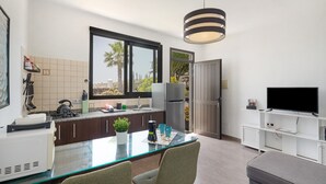 Una cocina moderna con una mesa de comedor de vidrio, un refrigerador, un televisor y un ventanal grande.