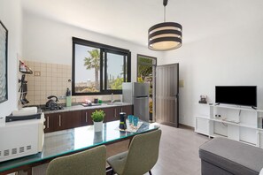 Een moderne keuken met een glazen eettafel, een koelkast, een televisie en een groot raam.