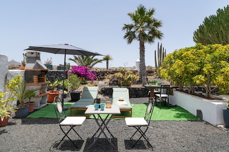 A patio with a table and chairs, surrounded by potted plants and a palm tree.. Vacation Home 'Volcanic House - in The Heart Of' with Shared Garden and Wi-Fi