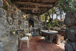 Un'area esterna con pareti in pietra, una panca di pietra, sedie in vimini e piante in vaso.