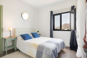 Una camera da letto con un letto, un comodino, una lampada, una finestra con tende e vista sul paesaggio.