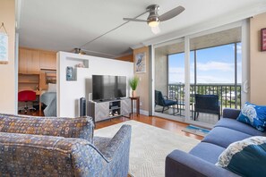 Ein modernes Wohnzimmer mit Flachbildfernseher, Deckenventilator und Balkon mit Sitzgelegenheit.