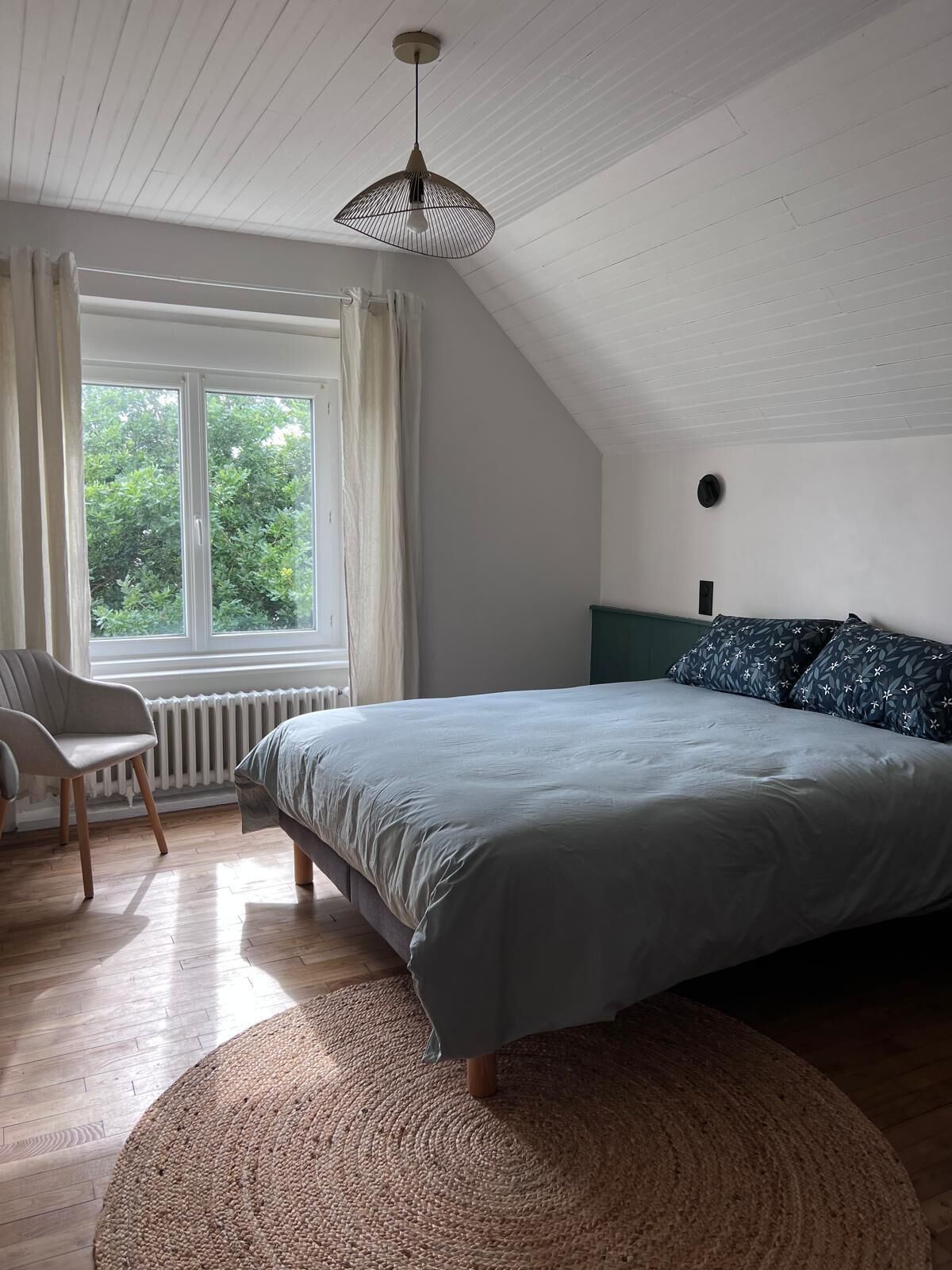 A bedroom with a bed, a chair, a window, and a ceiling fan.